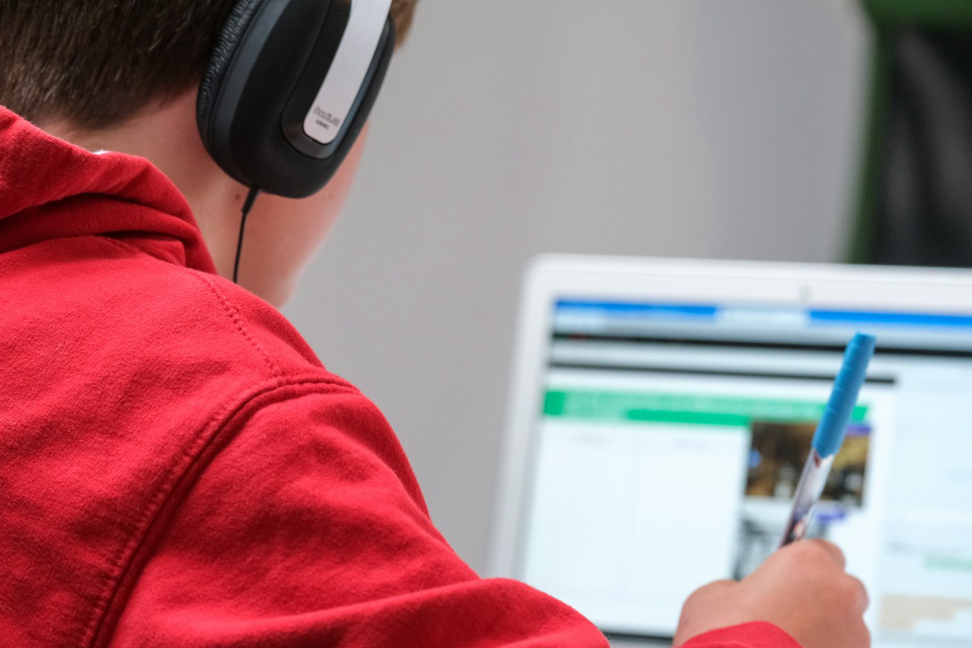 A learner in headphones follows a lesson on his laptop and takes notes
